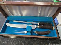 Open case showing knife, fork, steel with stag horn handles set in blue felt