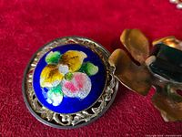 Front view of blue enamel round brooch adjacent to flower brooch