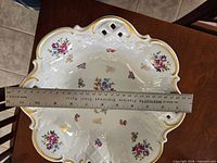 Top view with ruler showing approx 12 in width of scalloped porcelain bowl with floral pattern and gold trim.