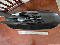 Top view of bowl containing carved utensils next to ruler