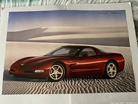 Front of poster showing red 2004 Corvette C5 coupe in desert scene with emblem