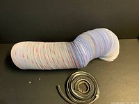 Coiled white vinyl duct and separate black foam strip on black surface