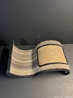 Angled view of the curved sisal cat scratcher showing carpet stripes and black trim