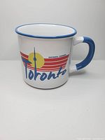 Front view of white mug with blue rim and handle, CN Tower Toronto graphic visible
