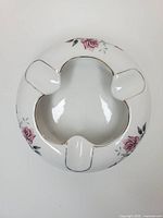 Top view of round porcelain ashtray showing three rests, floral decals and gold trim