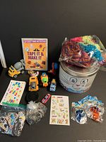 Overall view of lot showing tin, book, yarn loops, vehicles, stickers, pogs, sticky toys