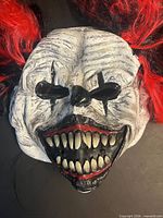 Front view of white scary clown mask with red hair and large teeth