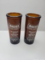 Two identical Sauza Conmemorativo Tequila brown glass shot glasses standing upright