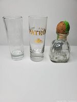 Two Patrón shot glasses and one miniature Patrón bottle standing side by side