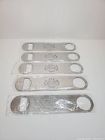 Five sealed Stella Artois metal bottle openers lined up