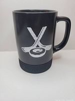 Front view of black Tim Hortons mug showing crossed sticks graphic and rubber puck base