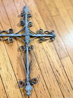 Full view of metal scrollwork cross on wooden floor