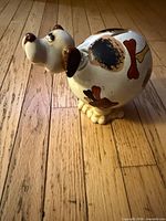 Left side view of cream ceramic dog piggy bank showing painted spots, bones and hearts