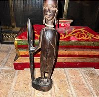 Full view of carved dark wood statue with spear and base