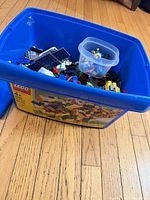 Blue LEGO storage bin containing loose LEGO pieces and small tub of minifigures