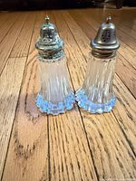 Two crystal shakers standing on wooden floor showing full form