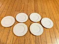 Six white milk glass plates laid out on wood floor