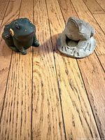 Concrete frog statue and painted ceramic frog figurine on wooden floor