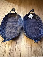 Two oval dark wicker trays with deer head handles displayed on floor, one with tag visible