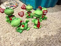 Five ceramic frog bobbleheads with heart signs on carpet