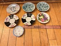 Overview of all seven small plates and saucers on wooden floor with ruler for scale