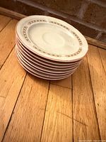 Stack of eight matching cream saucers showing rim and pattern