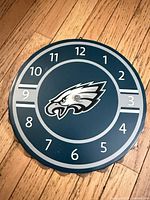Front view of metal Philadelphia Eagles clock face showing logo, numerals, missing hands