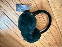 Full view of emerald green faux fur earmuffs with tag