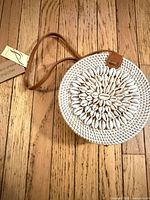 Front of round woven straw purse showing cowrie shell embellishment, strap, and attached tag