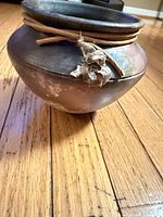 Front angled view of rounded ceramic vase showing smoky finish and leather cord with dried flower