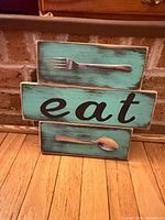 Front view of turquoise wooden sign showing fork, spoon and lettering