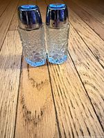 Two faceted crystal shakers standing side by side on wood floor