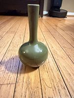 Full view of green ceramic bud vase standing upright on wood floor