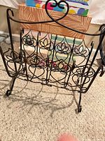 Front view of wrought iron magazine rack showing scrollwork, heart handle, lattice compartments, and curled feet