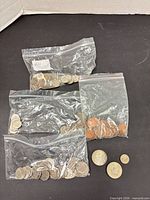 Four bags of mixed coins and several loose coins displayed on black background
