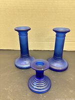Three cobalt blue glass candlesticks, two tall and one short, front view