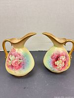 Front view showing both ewers with floral panels and gilt handles