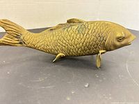 Side view of brass fish figurine showing scale texture, fins, and standing supports