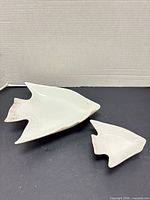 Large and small white ceramic fish-shaped dishes on black background