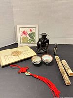 Group shot showing all items: wood figure, bone sheaths, tray, bowls, tassel, print, inlaid cylinder