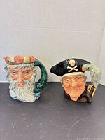 Front view of both Royal Doulton toby mugs showing designs and handles