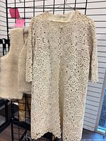 Full view of crochet jacket and wool vest hanging on grid