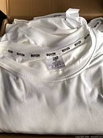 Stack of folded white BOYZN T-shirts in box showing collar branding