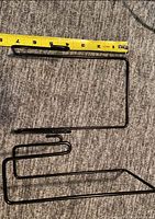 Black metal grid wall hook with measuring tape for scale, shows approximate length and design