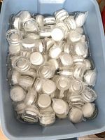 Blue bin filled with individually wrapped clear glass cosmetic jars with white lids