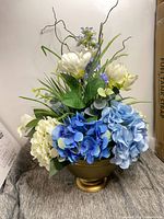 Front view of the artificial floral arrangement showing blue and white hydrangeas, white lilies, purple delphinium and greenery in gold pedestal bowl