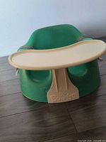 Front view of green Bumbo seat with tray attached