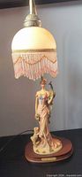 Lamp lit showing glass dome shade, beaded fringe, figure, wood base