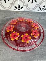 Top view of red circular hummingbird feeder showing flower ports and perch ring, still in shrink wrap