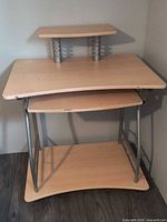 Full view of light beech laminate computer desk showing main top, raised monitor shelf, keyboard tray and lower shelf